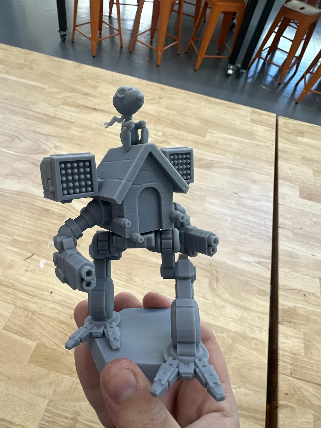 An unpainted miniature statuette of Snoopy's doghouse, from the Peanuts comic strip, fused to the chassis of a Timber Wolf OmniMech from the BattleTech tabletop wargame. Snoopy himself is sitting on top of the doghouse, as he often does, wearing his full World War Flying Ace garb; flight hat and goggles, and scarf. The doghouse completely replaces the torso region of the Timber Wolf, albeit with all its weaponry still visible on the house. 

The size of the statuette is ambiguous, but nonetheless apparently too large to be practical on a typical BattleTech playmat.